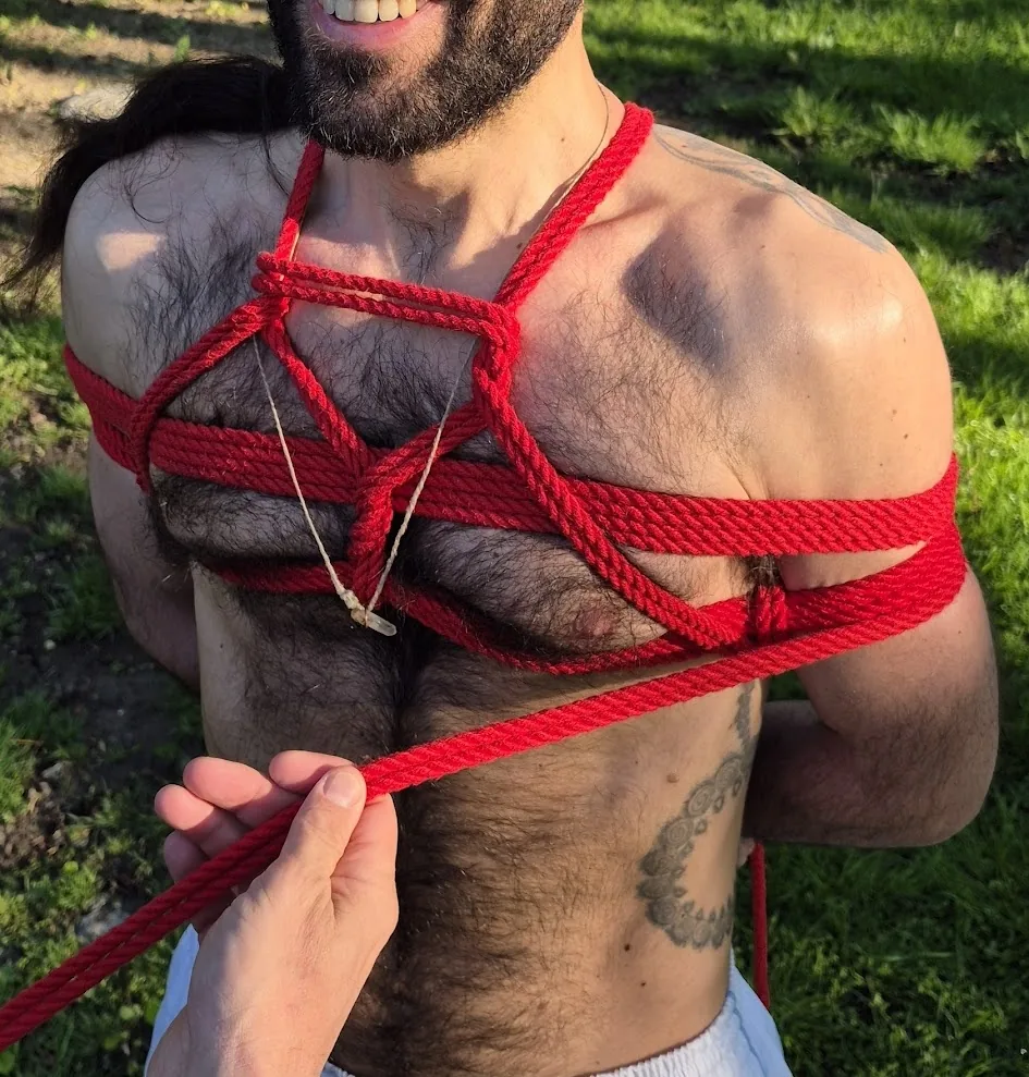 Red rope across the chest, seen close up, with a hand guiding the rope
