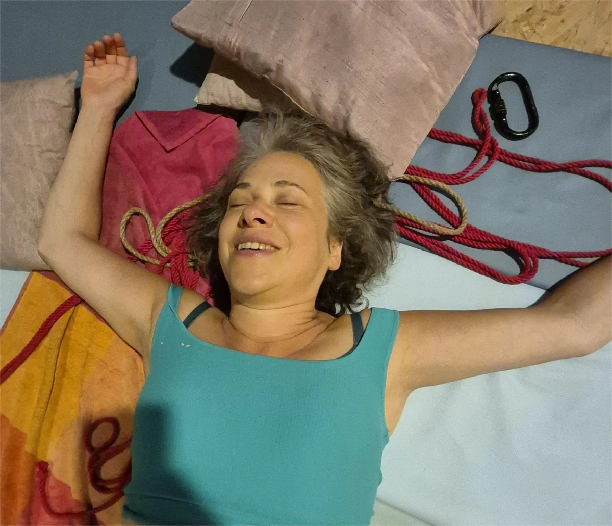 Someone lying relaxed on cushions with arms spread, rope beside them